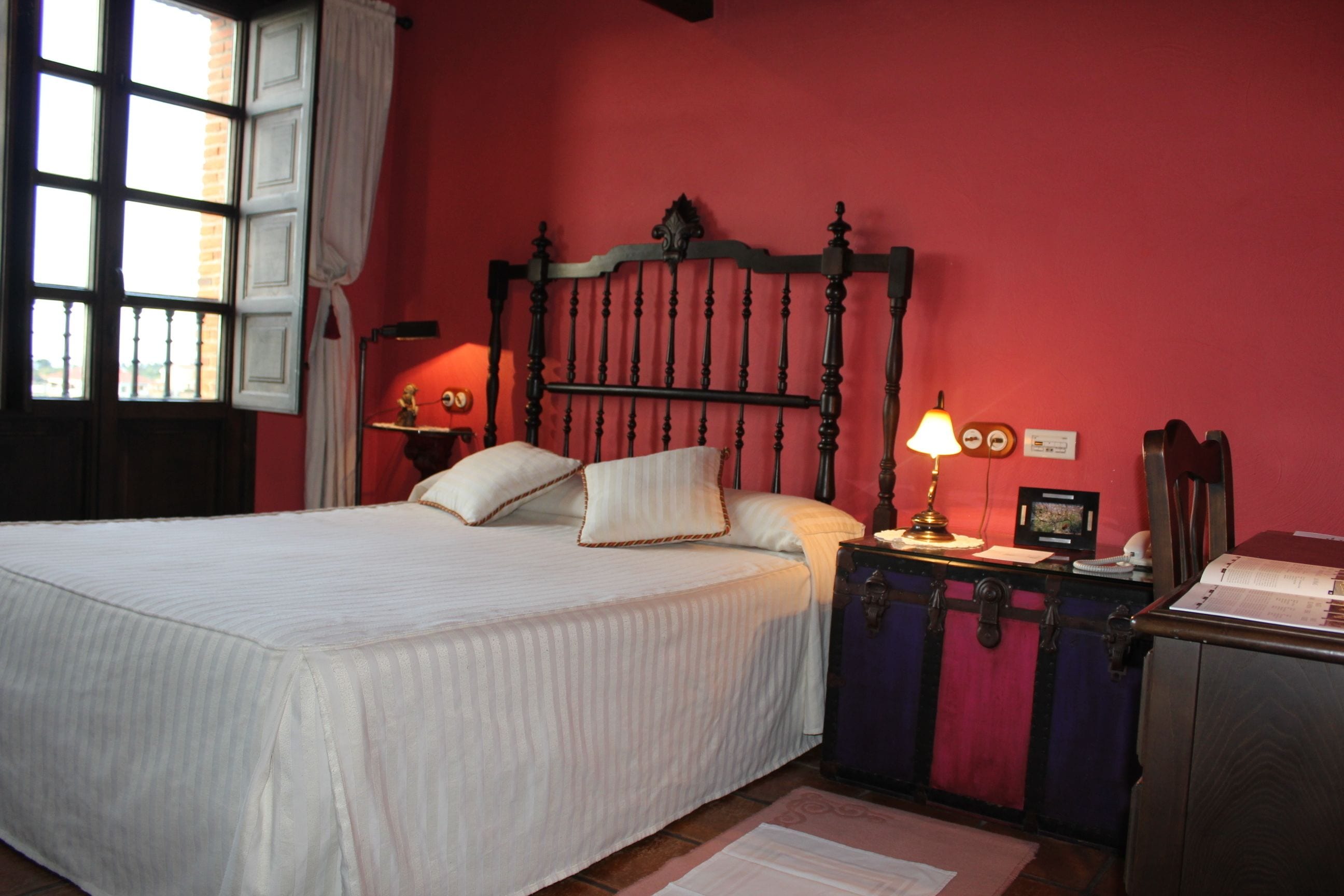 Un dormitorio con cama, mesita de noche con lámpara, cómoda y ventana con cortinas.