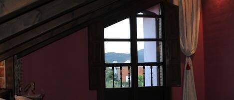 A bedroom with a bed, a chair, a window with curtains, and a view of the outdoors.