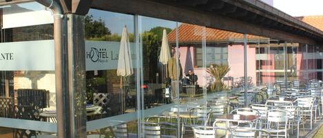 An outdoor cafe with tables and chairs, a covered seating area, and a building with a sign that reads "HOTEL La Plage".