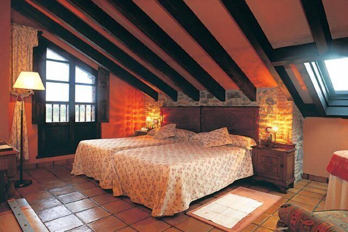 Um quarto de sótão aconchegante com teto inclinado, uma cama com roupa de cama florida, uma mesa de cabeceira e um abajur.