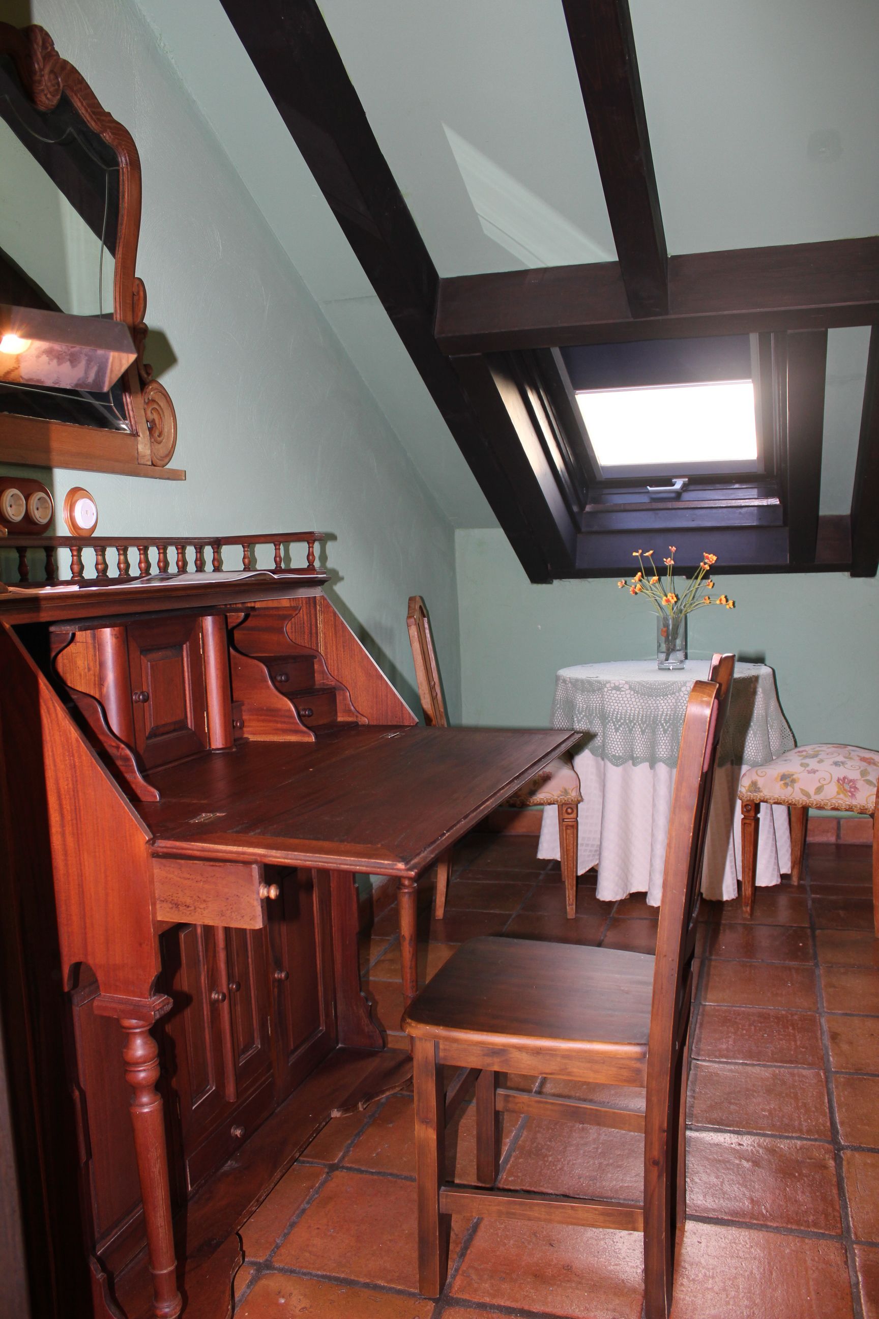 A dining area with a wooden table and chairs, a small round table with a vase of flowers, and a skylight above.