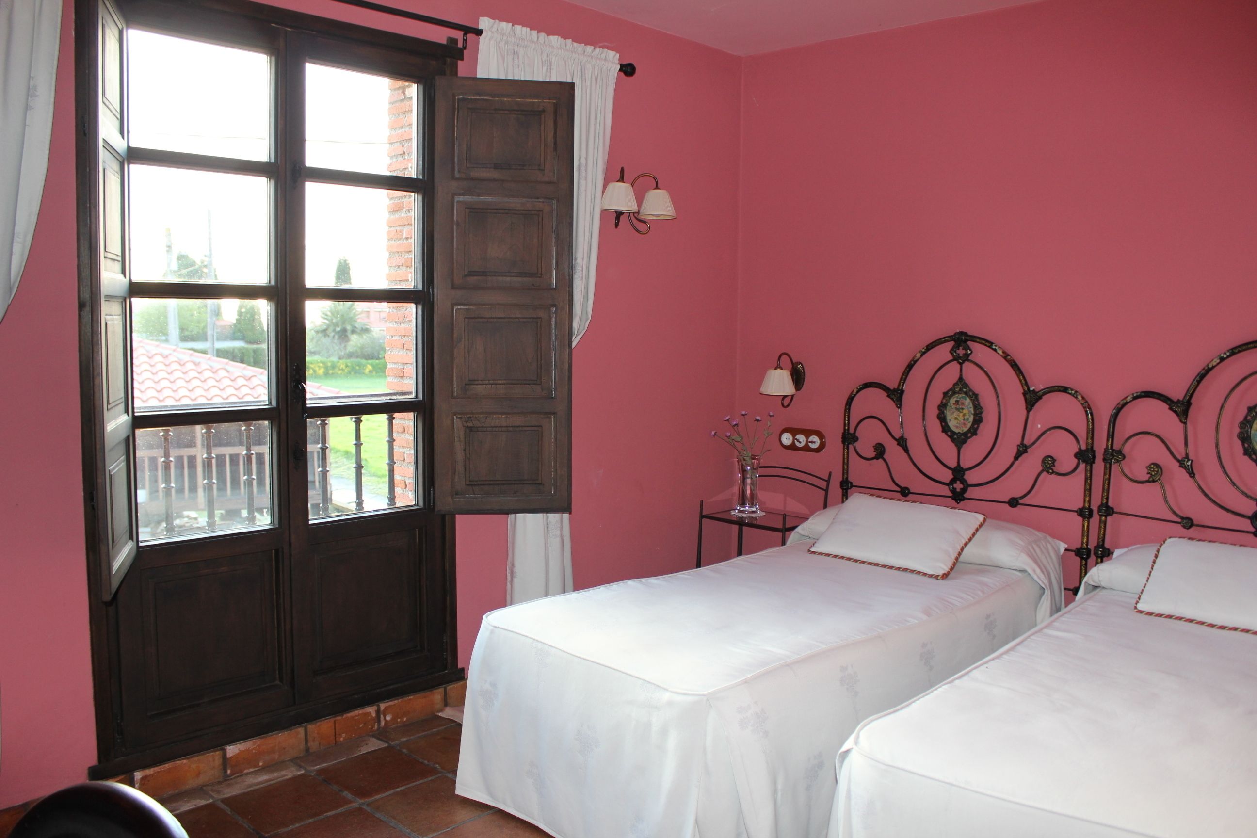 A bedroom with two beds, a window with curtains, and a view of a garden.