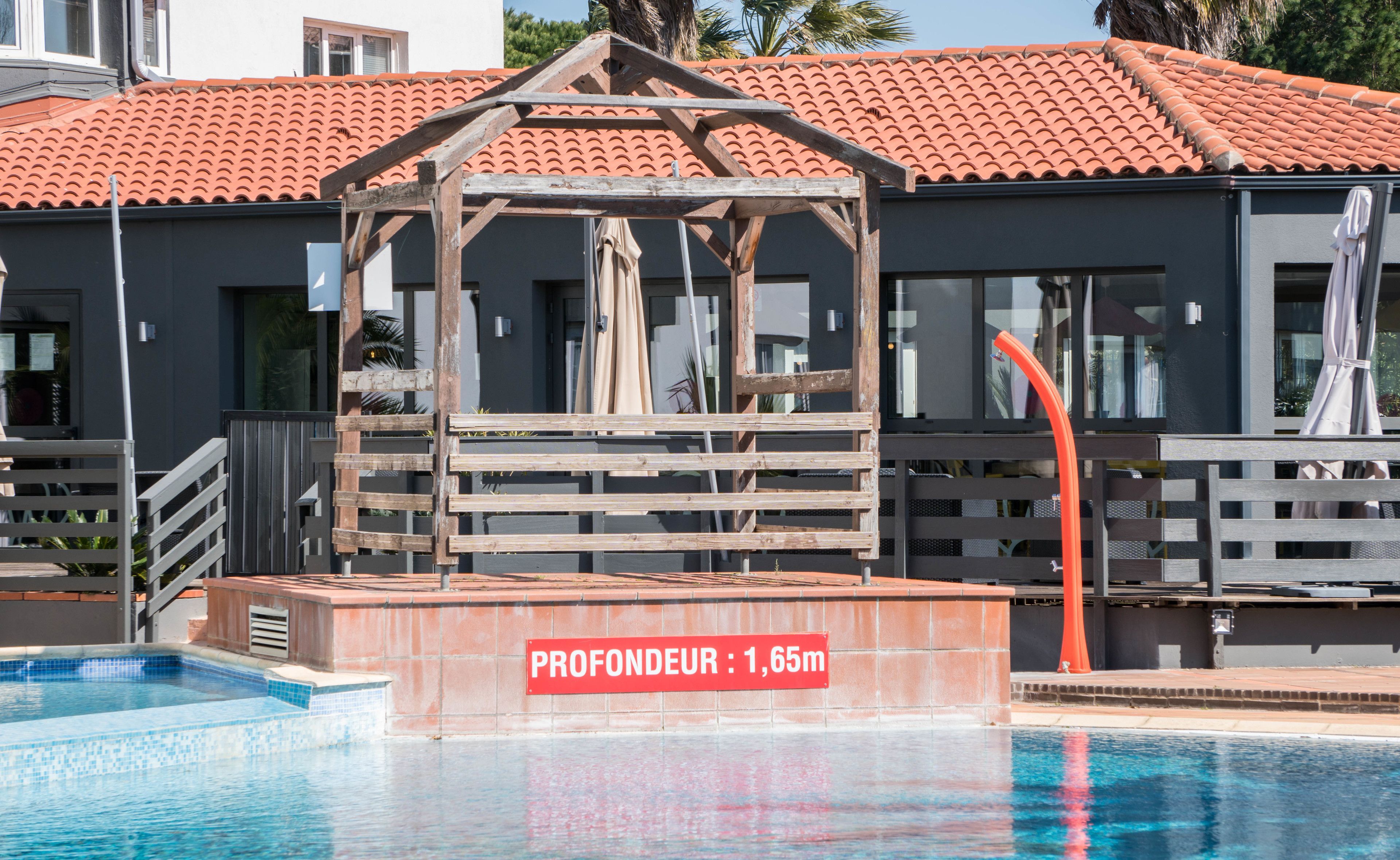 A swimming pool with a wooden structure and a sign indicating a depth of 1.65 meters.