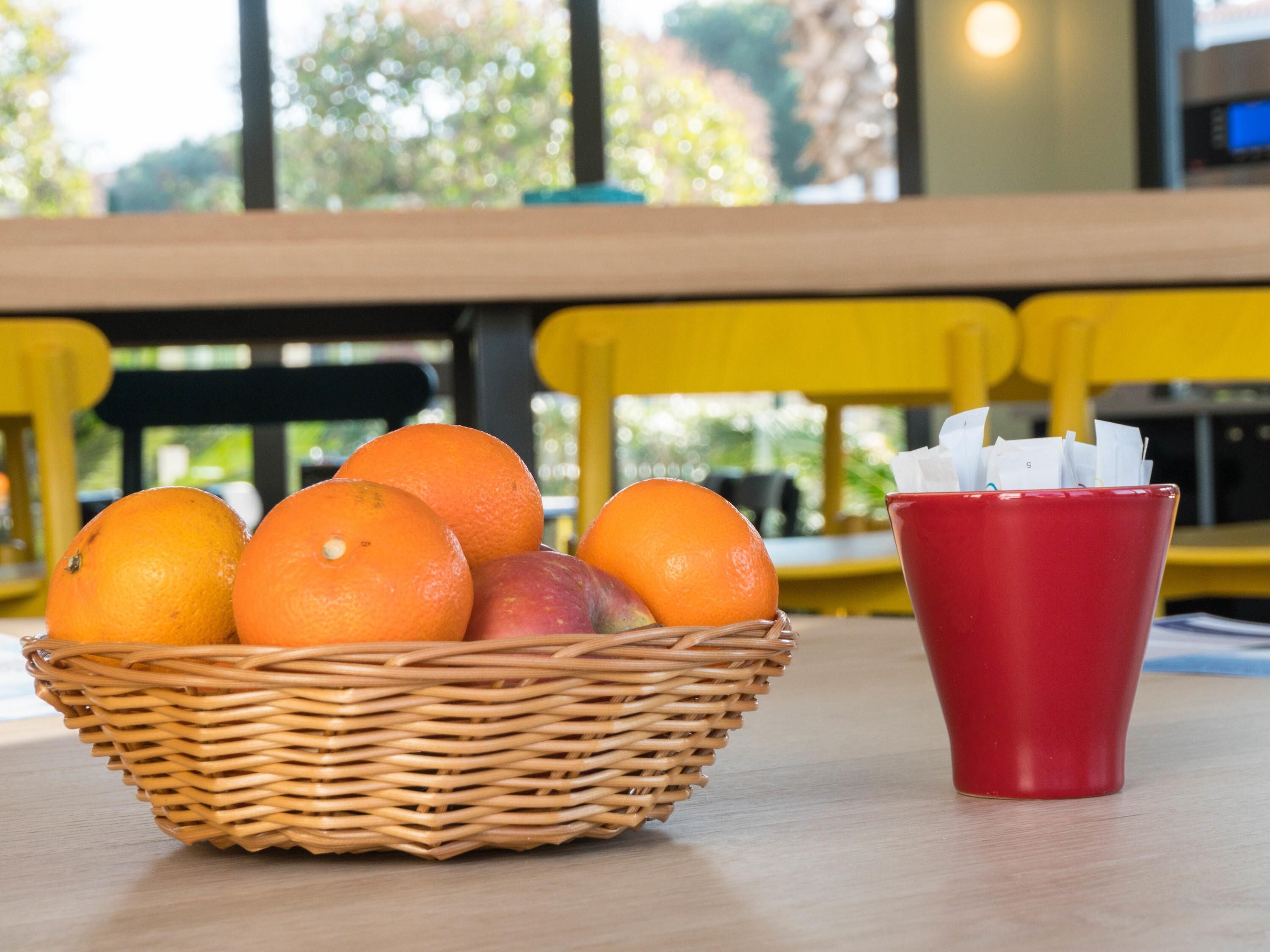A wicker basket with oranges and a red cup on a table.