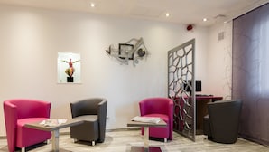 A modern waiting area with two pink chairs, a grey chair, and a small table with magazines. - Kyriad Nancy Sud - Ludres (Ludres)