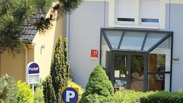 Un edificio con un'insegna per il parcheggio, un ingresso con porta in vetro e una segnaletica che indica 'Kyriad'.