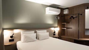 A hotel room with a bed, bedside tables, an air conditioning unit, a mirror, and a coat rack. - Kyriad Nancy Sud - Ludres (Ludres)