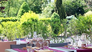An outdoor dining area with tables set for a meal, surrounded by lush greenery and trees. - Kyriad Nancy Sud - Ludres (Ludres)