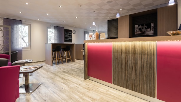A modern interior with a reception desk, wooden flooring, and a mix of seating areas. - Kyriad Nancy Sud - Ludres (Ludres)