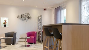 A modern interior with a wooden bar area, two chairs, a pink chair, and a grey chair. - Kyriad Nancy Sud - Ludres (Ludres)