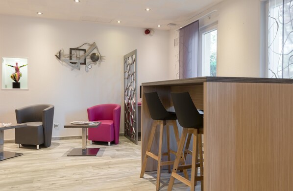 A modern interior with a wooden bar area, two chairs, a pink chair, and a grey chair. - Kyriad Nancy Sud - Ludres (Ludres)