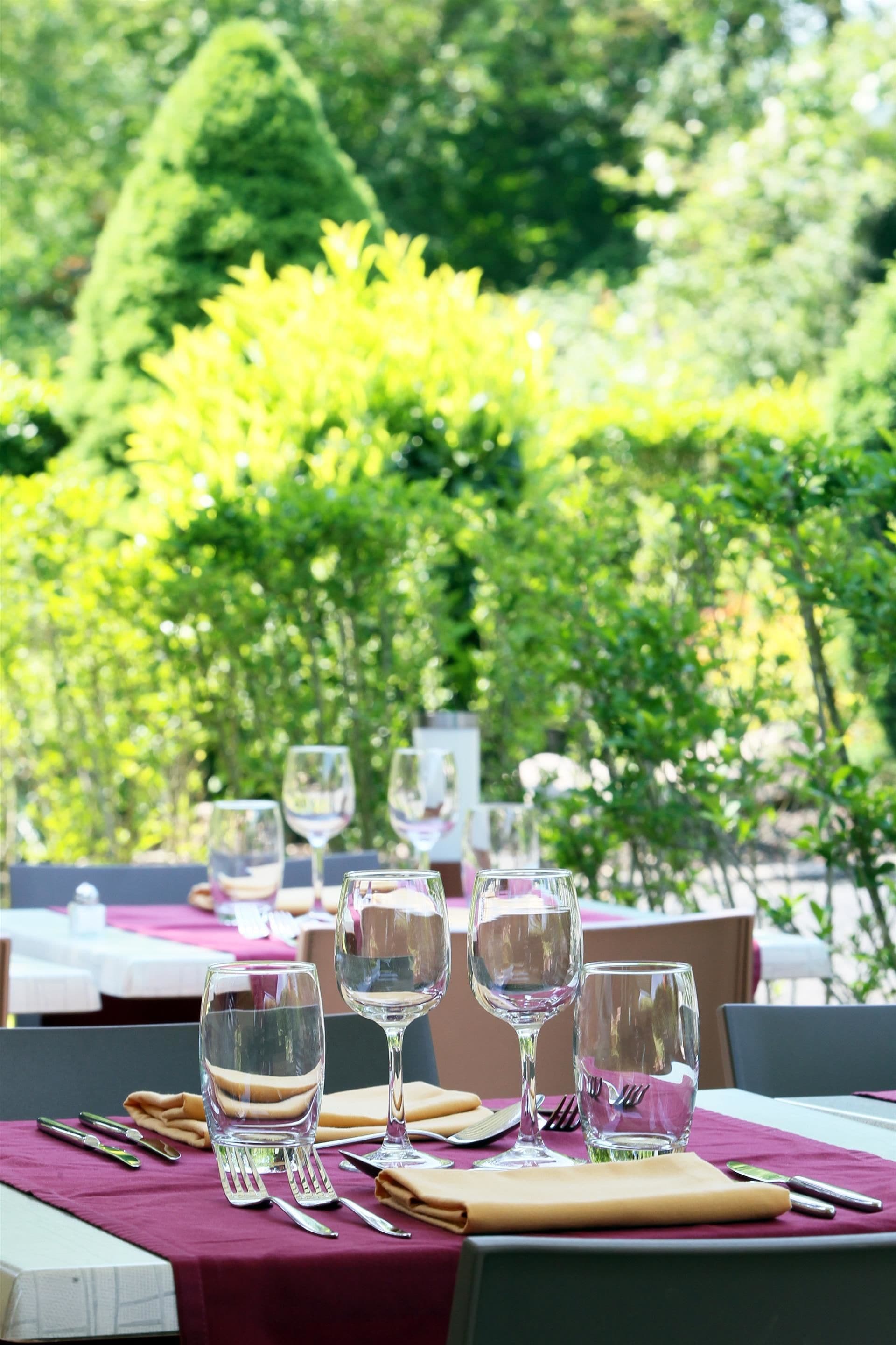 An outdoor dining area with tables set for a meal, surrounded by lush greenery.