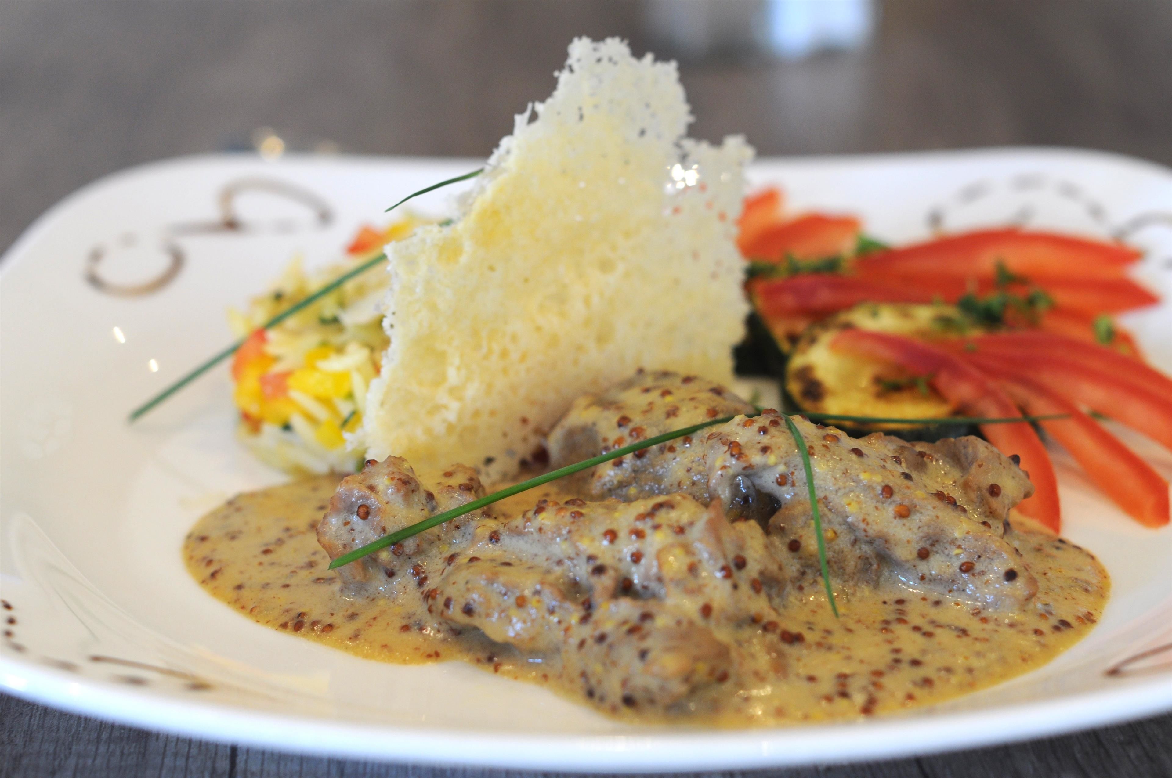 Une assiette comprenant un plat de viande, un petit pain et une portion de légumes coupés en tranches.