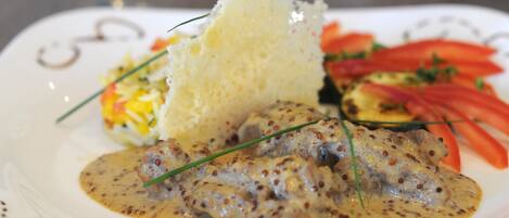 Une assiette comprenant un plat de viande, un petit pain et une portion de légumes coupés en tranches.