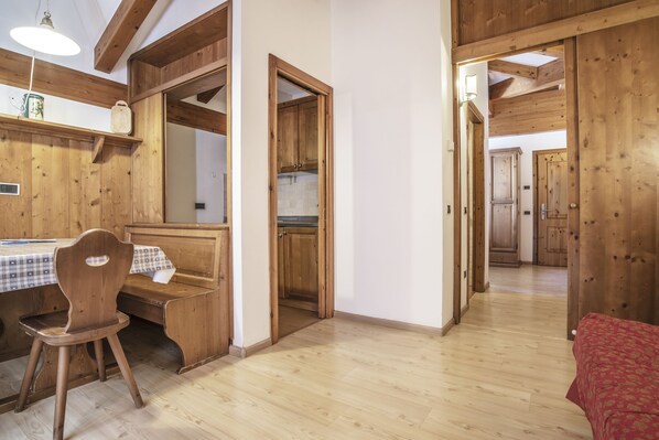 Un interior de madera con una mesa y sillas de comedor, una zona de cocina y un pasillo que conduce a otra habitación.