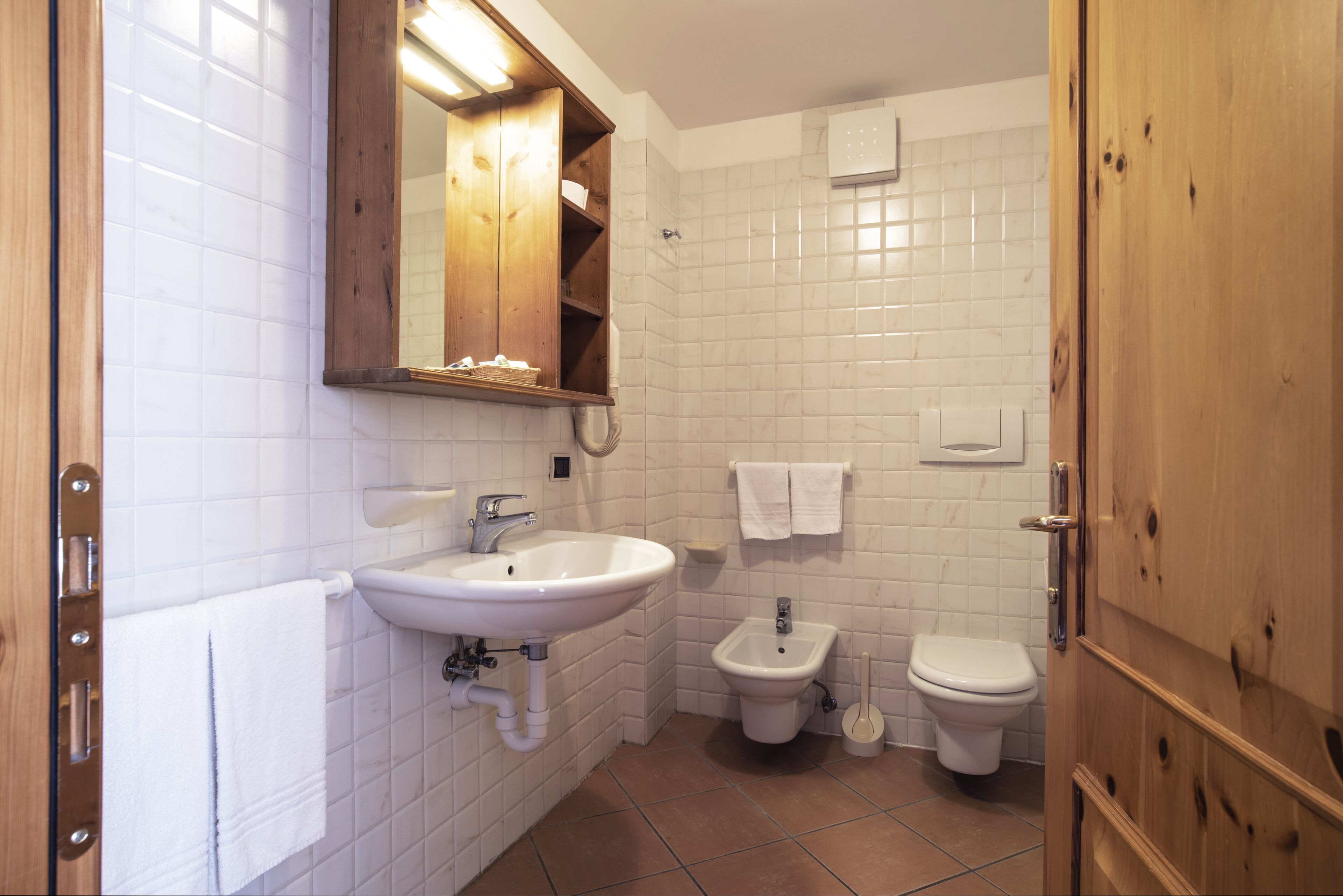 A bathroom with a sink, bidet, toilet, and wooden cabinets.