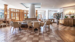 A spacious dining area with wooden tables and chairs, large windows, and a central column. - Sporting Clubresidence (Primiero San Martino di Castrozza)