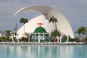 A modern building with a curved white roof, a green dome, and a red fish symbol on top. - Nautico (Santa Cruz de Tenerife)