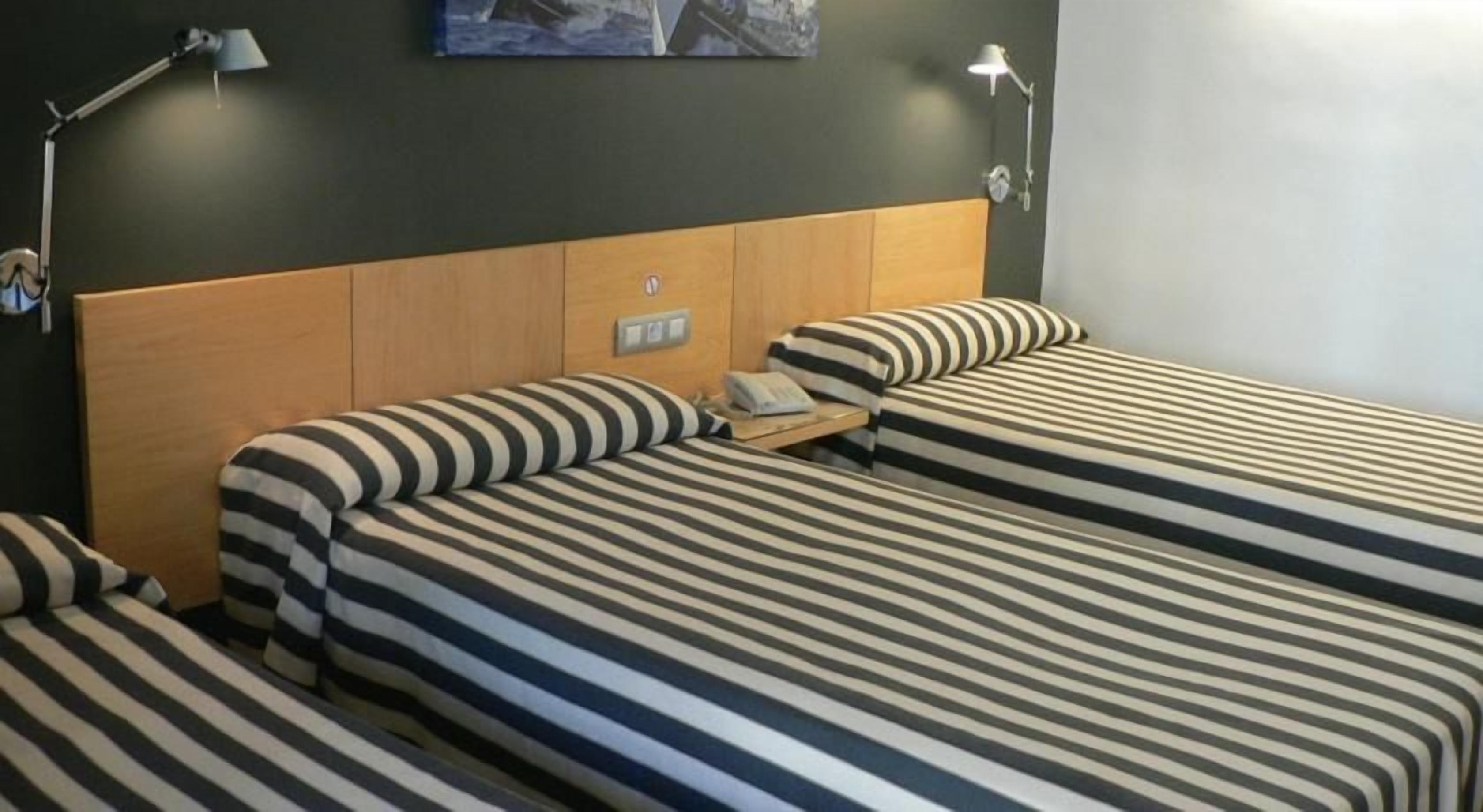 Une chambre d’hôtel avec deux lits, une tête de lit en bois, des lampes de chevet et un téléviseur à écran plat fixé au mur.