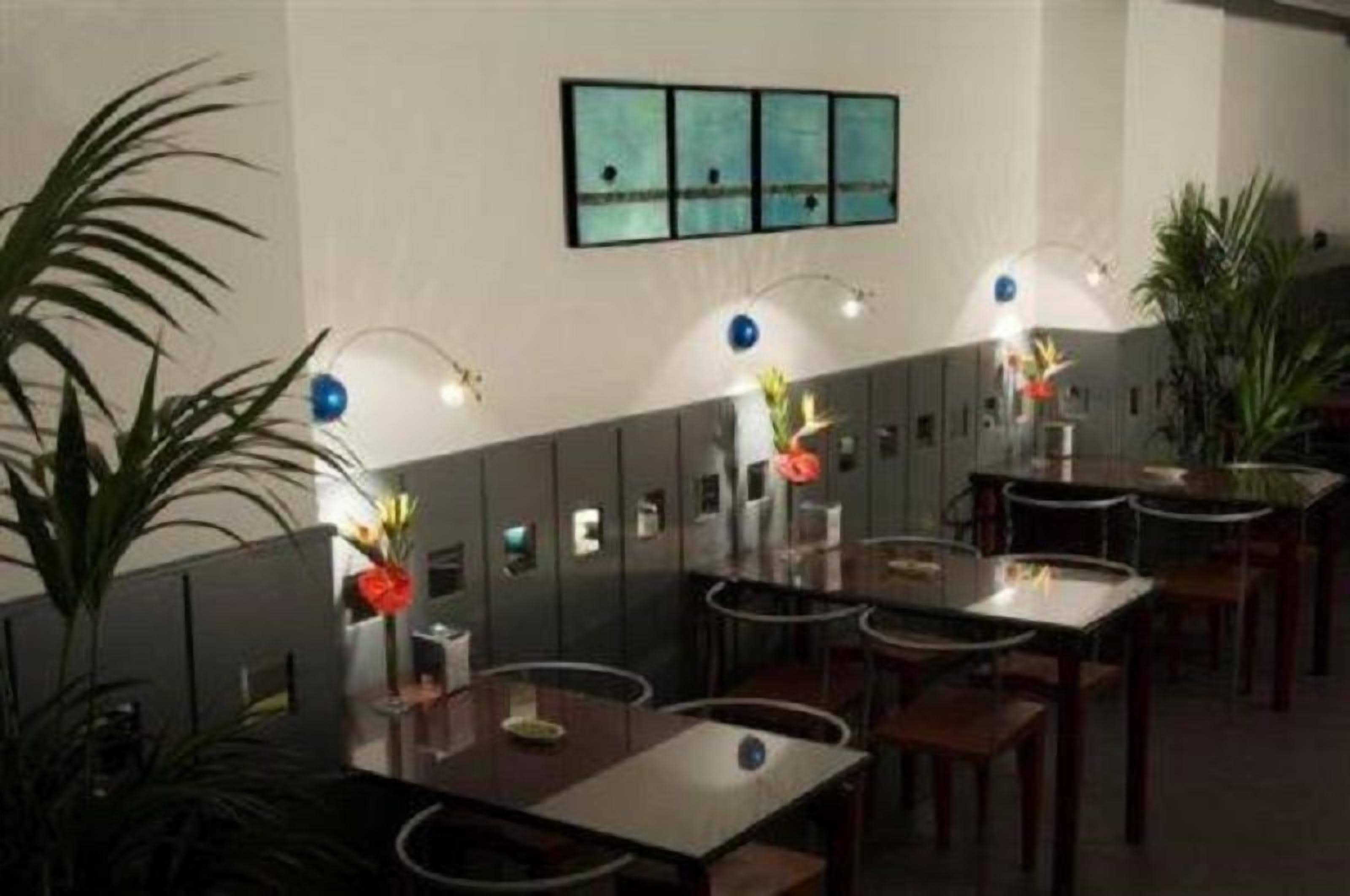 Un restaurant avec des tables et des chaises, des luminaires fixés au mur et des plantes en pot.