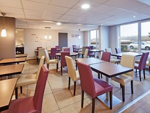 A modern restaurant interior with multiple tables and chairs, a visible kitchen area, and large windows offering a view of the outside. - Kyriad Auxerre - Appoigny (Appoigny)