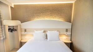 A hotel room with a large bed, two bedside tables, a built-in shelf, and a shower area. - Kyriad Auxerre - Appoigny (Appoigny)