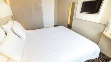 A hotel room with a bed, a TV mounted on the wall, and a bathroom visible through an open door.