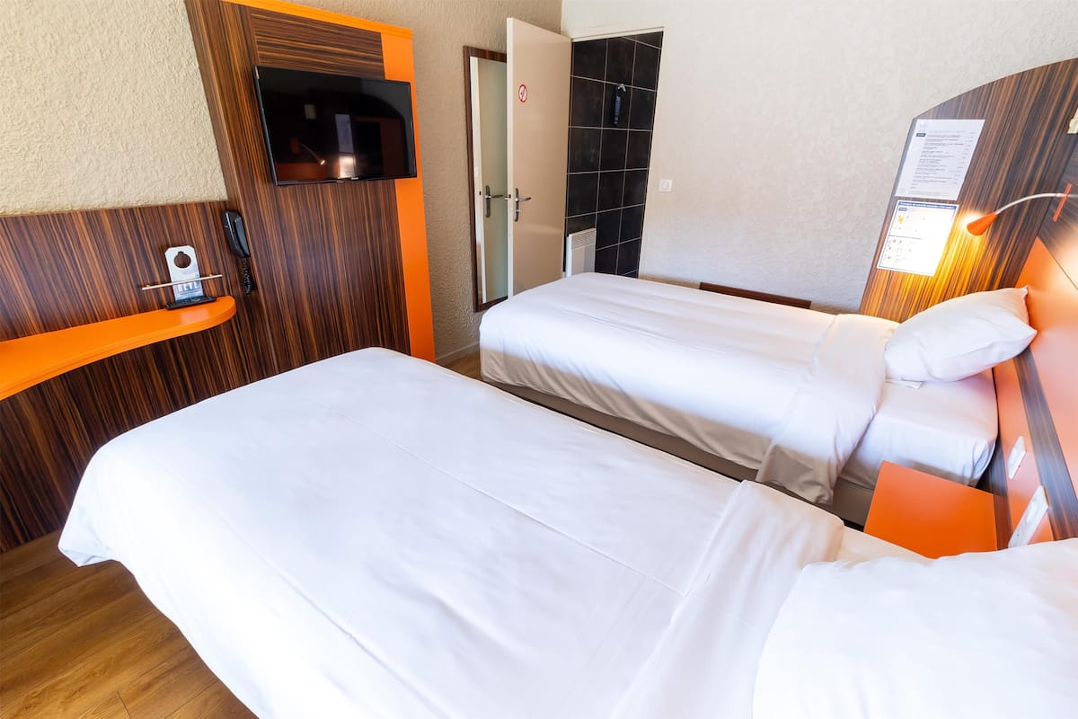 A hotel room with two beds, a TV, a phone, and a door with a no-smoking sign.