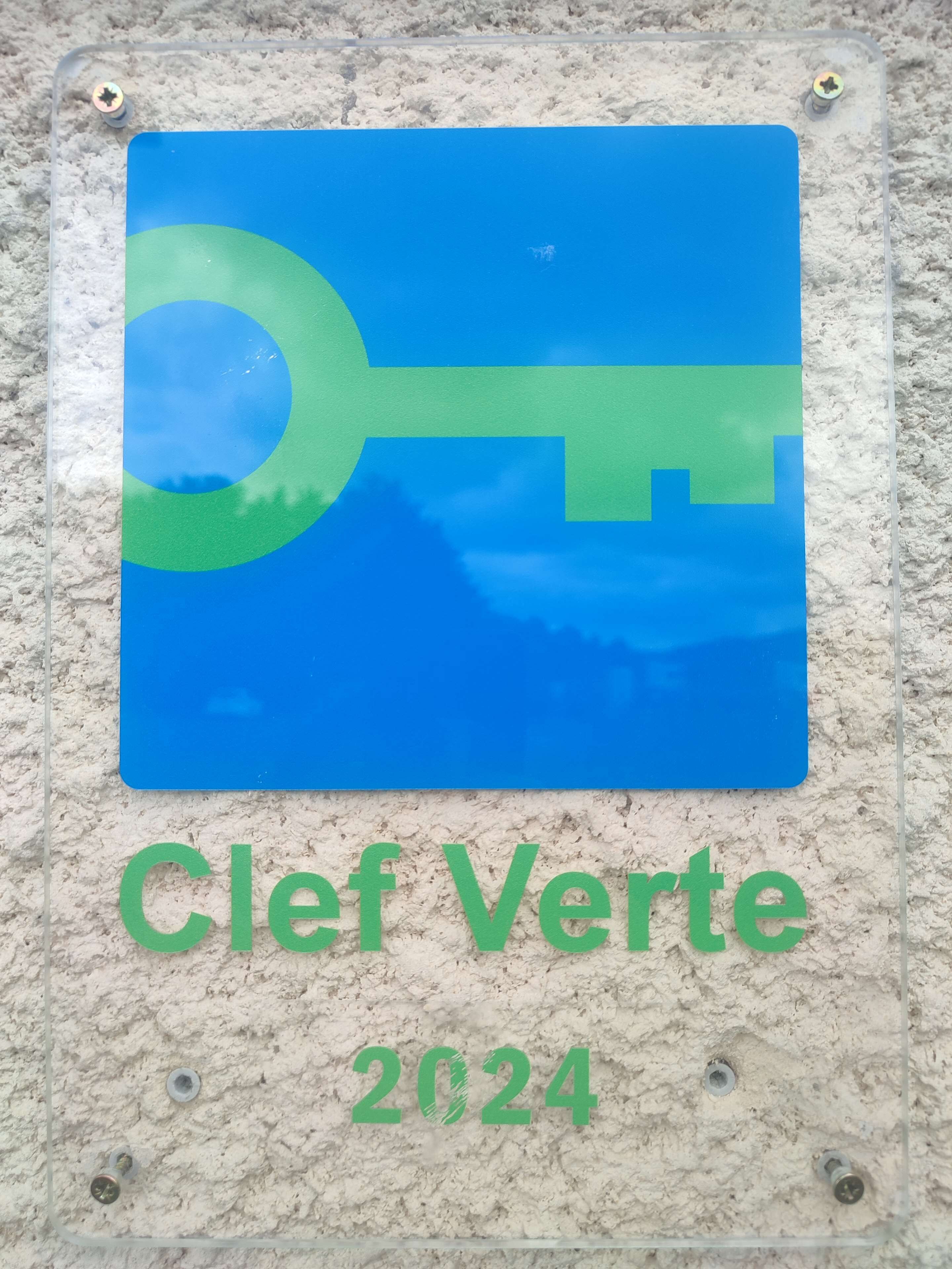 Un letrero con un gráfico de llave y el texto 'Clef Verte 2024' montado sobre una pared con textura.