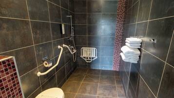 A modern bathroom with dark tiles, a white toilet, a shower with a handheld showerhead, and a towel rack with neatly folded towels.