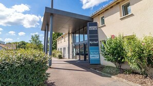 A building entrance with a sign reading "Bienvenue Chez Kyriad DIRECT" and a covered walkway. - Kyriad Auxerre - Appoigny (Appoigny)