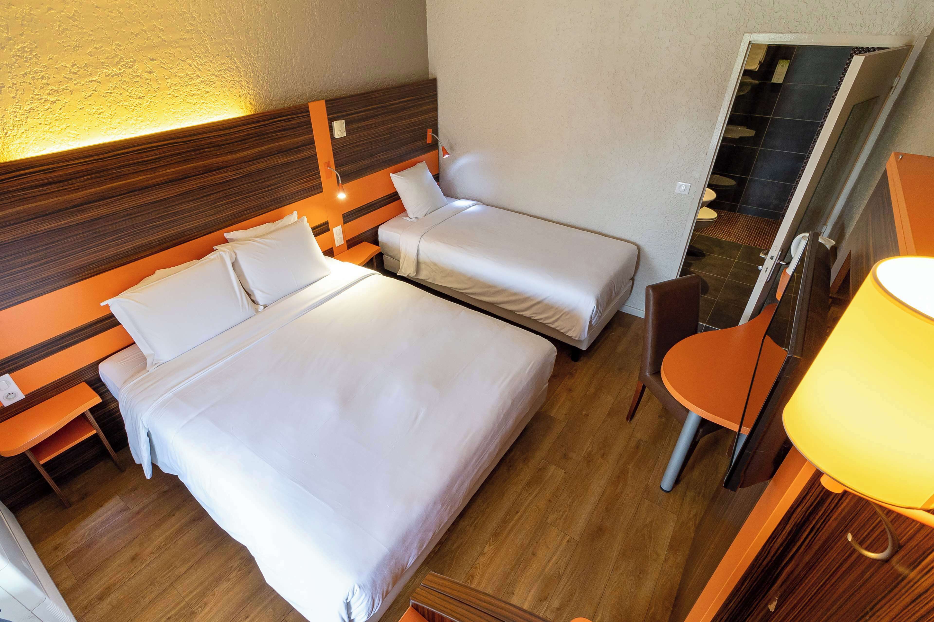 A hotel room with two single beds, a wooden headboard, a desk with a chair, and a bathroom visible through an open door.
