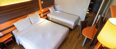 Een hotelkamer met twee enkele bedden, een houten hoofdbord, een bureau met een stoel, en een badkamer zichtbaar door een geopende deur.