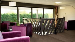 A modern office space with purple upholstered chairs, a wooden partition, and large windows offering a view of greenery. - Kyriad Auxerre - Appoigny (Appoigny)