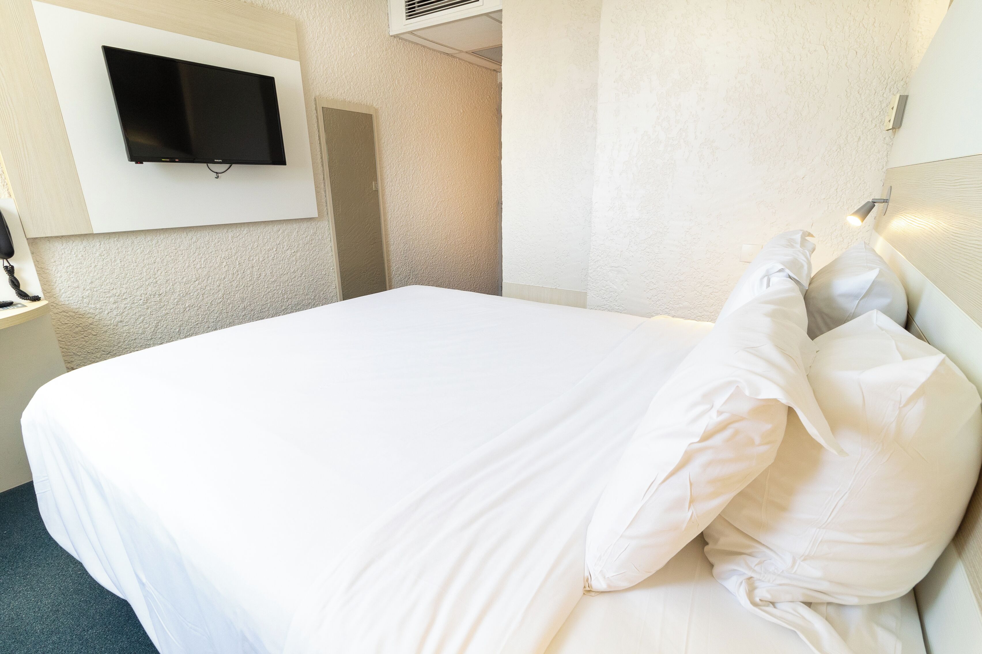 Camera d'albergo con un letto grande, una TV a parete e un comodino con una lampada.