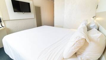 Camera d'albergo con un letto grande, una TV a parete e un comodino con una lampada.