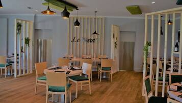 A restaurant interior with wooden furniture, green cushioned chairs, and hanging pendant lights.