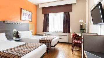 Habitación de hotel con dos camas, un escritorio, una silla, un televisor y una ventana con cortinas.