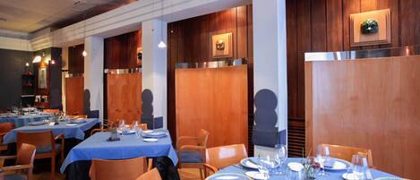 Ein Restaurant mit mehreren gedeckten Tischen, blaue Tischdecken und Holzvertäfelung an den Wänden.