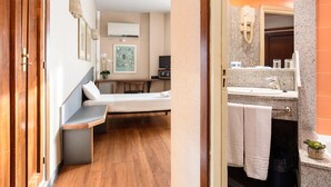 Habitació d'hotel amb llit, taula de nit i bany que inclou un lavabo i un mirall.