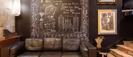 Un sofá de cuero marrón oscuro en una habitación con una pared grande cubierta de una pizarra, mostrando citas e ilustraciones.