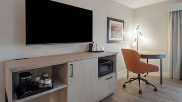 Quarto de hotel com televisão de tela plana, cafeteira, micro-ondas, escrivaninha, poltrona laranja e abajur.