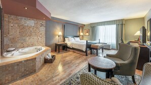 Habitación de hotel con una bañera grande, una cama con sábanas blancas, una mesita y dos sillones.
