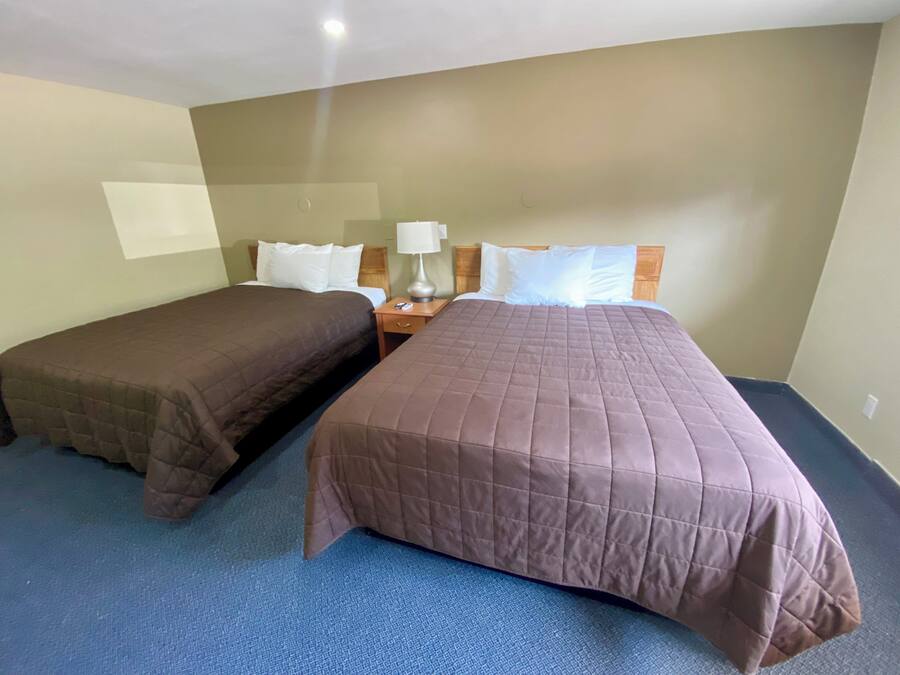 A hotel room with two beds, a nightstand, and a lamp.