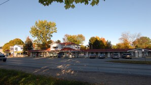 A motel with a red roof, a diner across the street, and a parking lot with several cars. - Kings Inn - Orillia (Orillia)