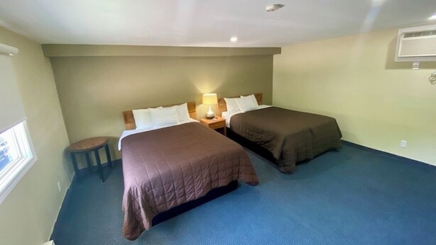 A room with two beds, a small stool, a nightstand with a lamp, and a window. - Kings Inn - Orillia (Orillia)