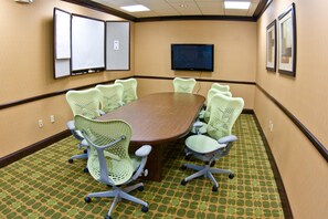 Un salón de conferencias con una gran mesa ovalada rodeada por seis sillas de malla verde con ruedas.