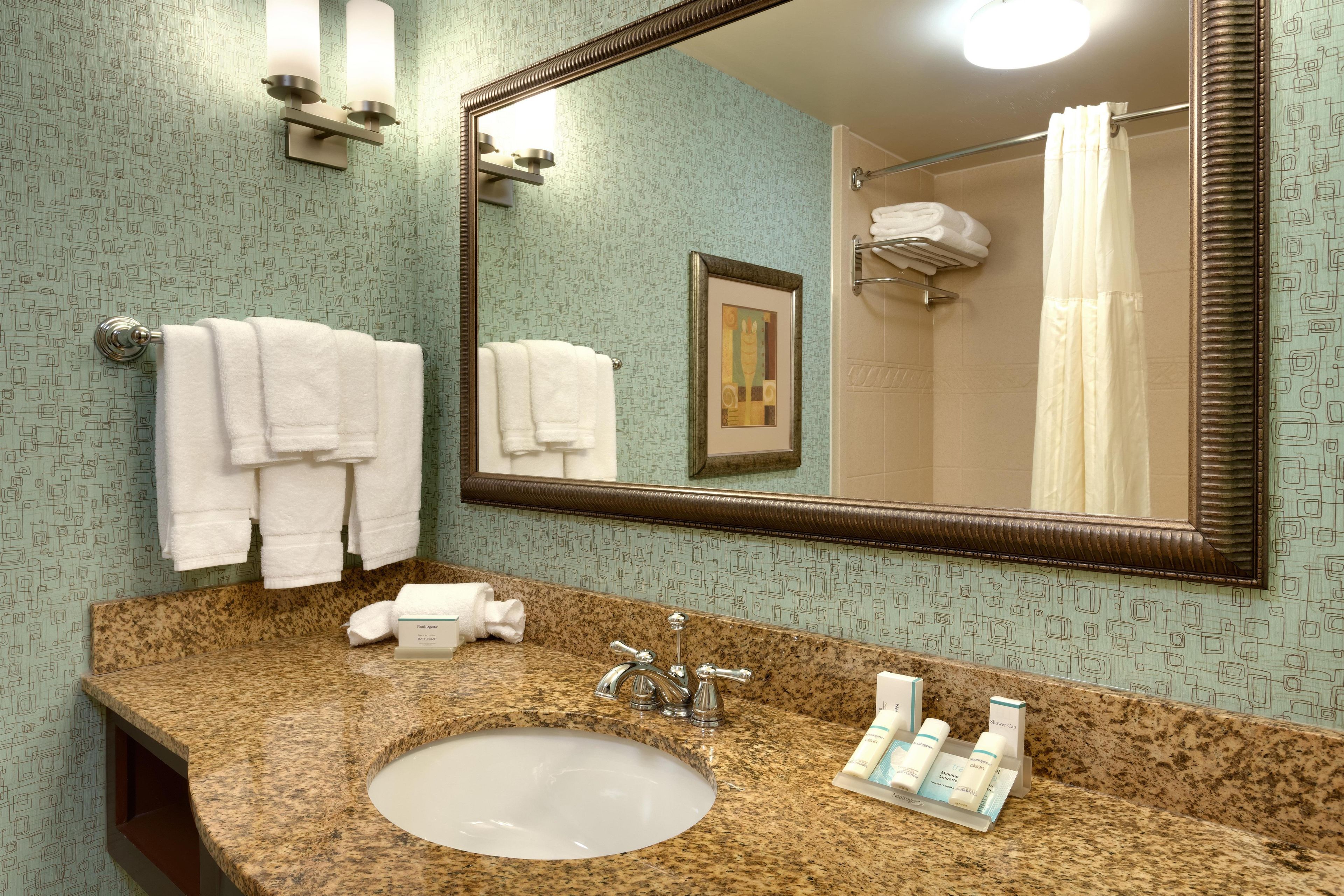 A bathroom with a granite countertop, a sink, a mirror, and a towel rack with multiple towels.