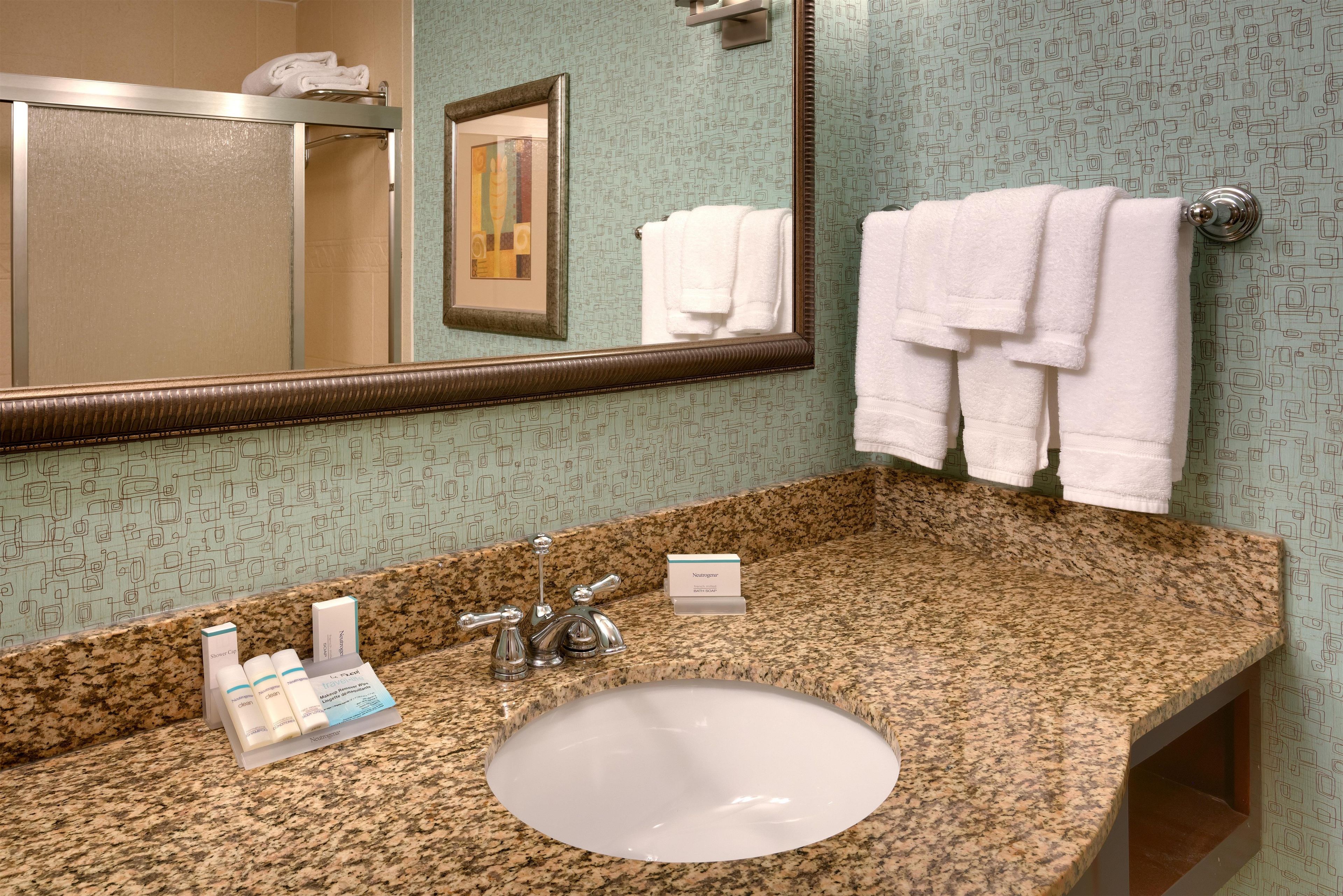 A bathroom with a granite countertop, a sink, a mirror, and a towel rack with towels.