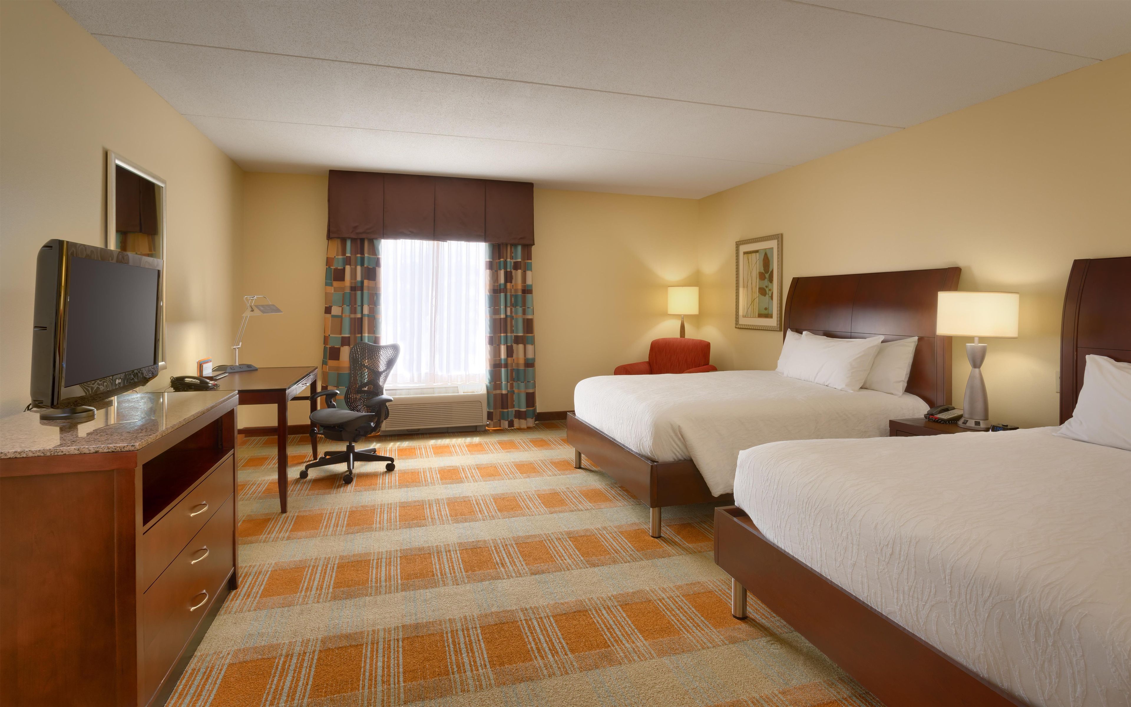A hotel room with a bed, a desk, a chair, a television, and a window with curtains.